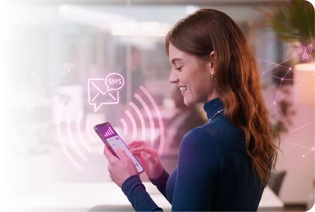 Joven mujer con cabello castaño rojizo sonriendo ante su smartphone con íconos digitales brillantes - un sobre de correo electrónico, una burbuja de SMS y ondas de señal Wi-Fi - flotando alrededor del dispositivo